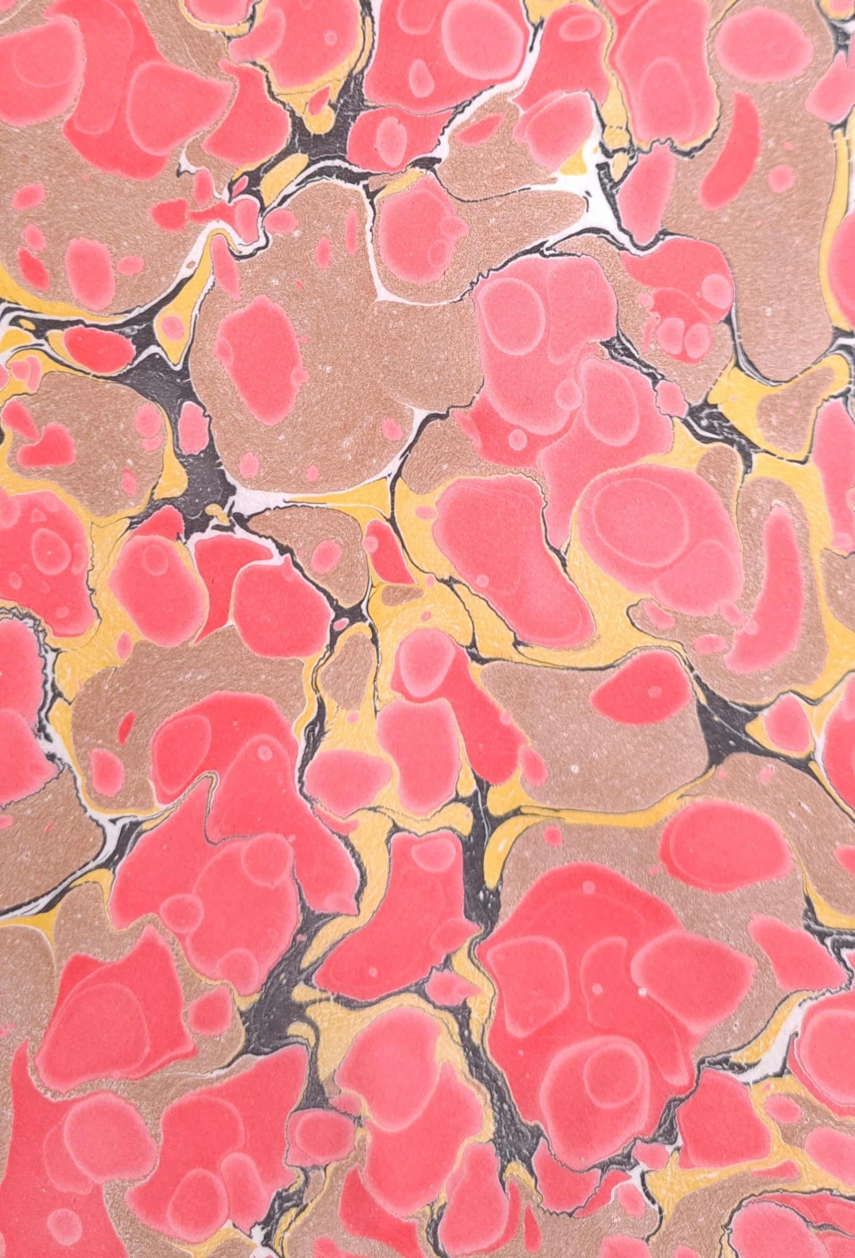 A piece of handmade marbled paper with a watercolour based marbling pattern of red spots, warm yellow and black veins on an earthy light brown background.